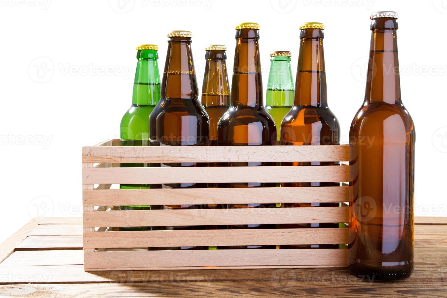de nombreuses bouteilles en verre de différentes bières sur une boîte en bois sans étiquette isolée, photo de différentes bouteilles de bière pleines sans étiquette. chemin de détourage séparé pour chaque bouteille inclus.
