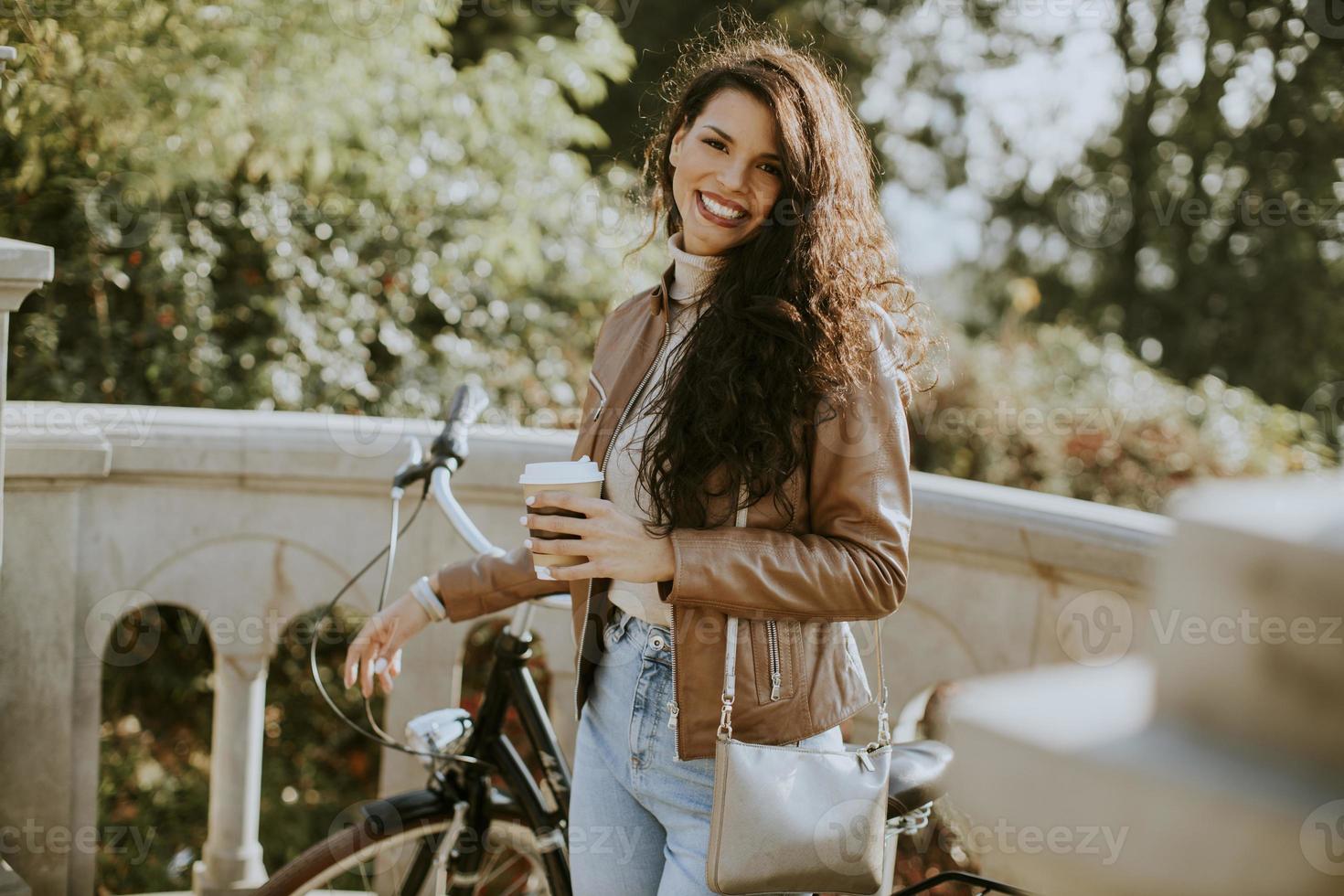 Jeune femme tenant une tasse de café à emporter par le vélo le jour de l'automne photo