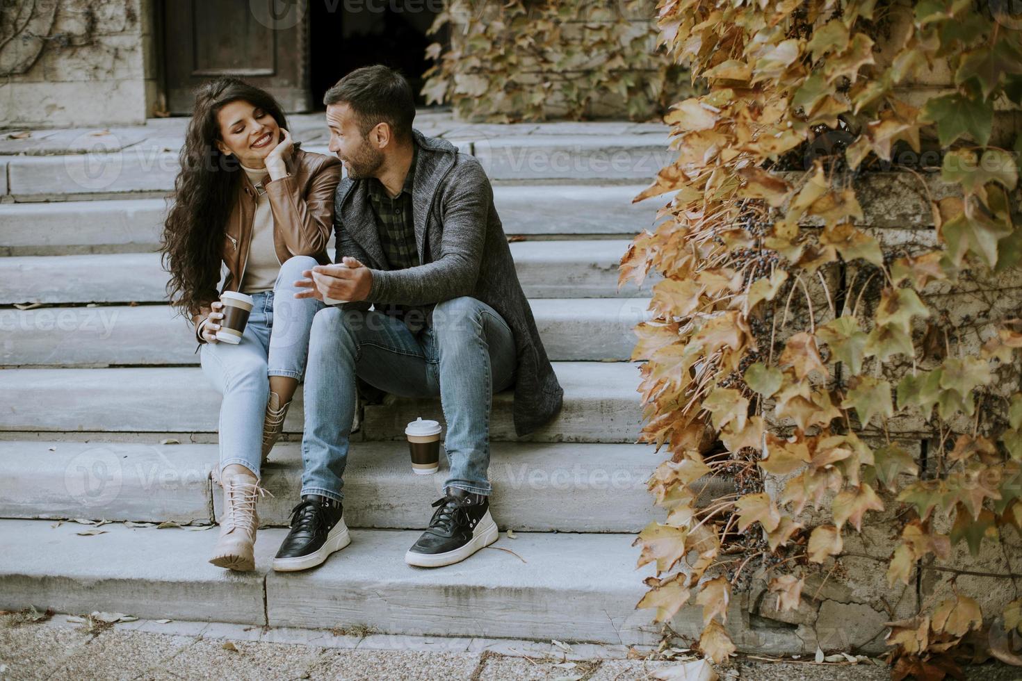 jeune couple assis sur des escaliers extérieurs un jour d'automne et utilisant un téléphone portable photo