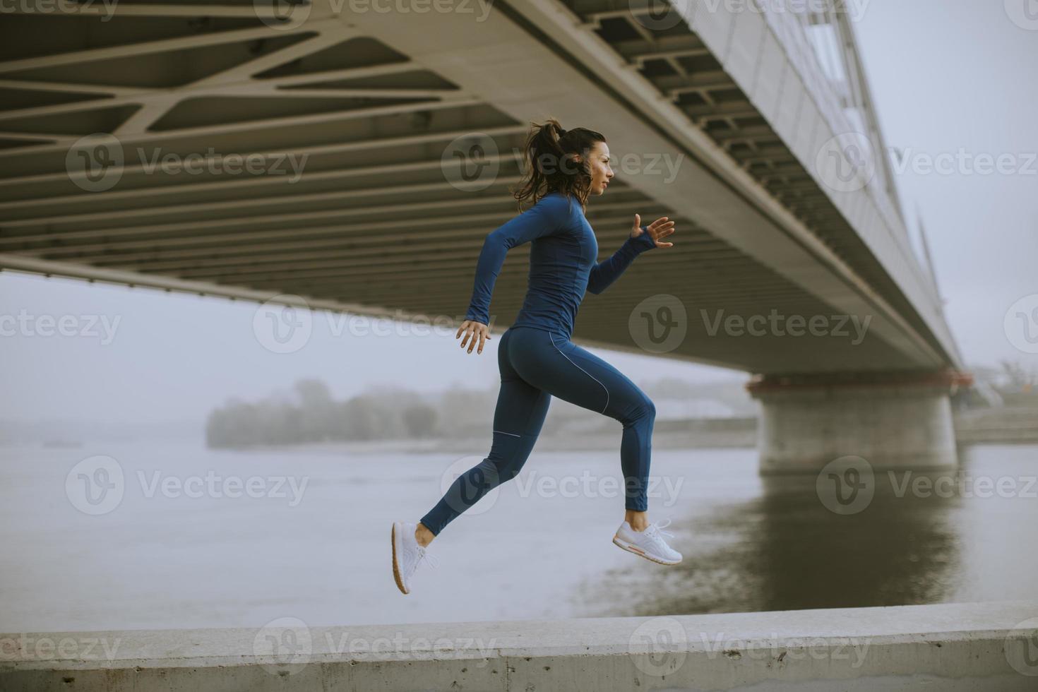 Jeune femme en survêtement bleu courant au bord de la rivière au matin d'automne photo