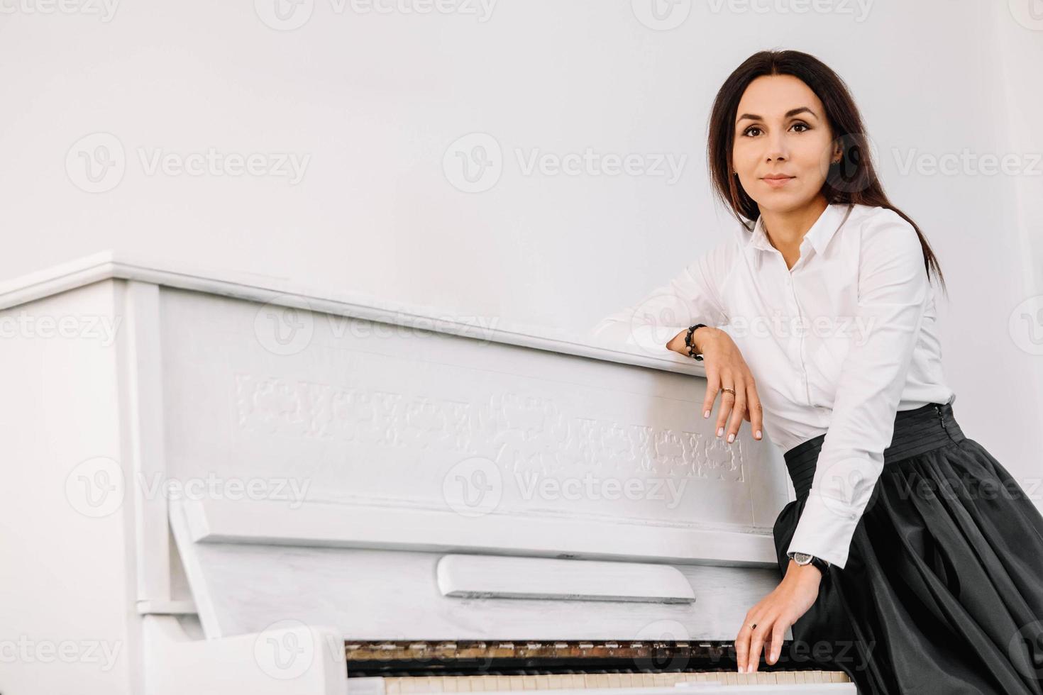 belle femme vêtue d'une chemise blanche jouant sur un piano blanc. place pour le texte ou la publicité photo