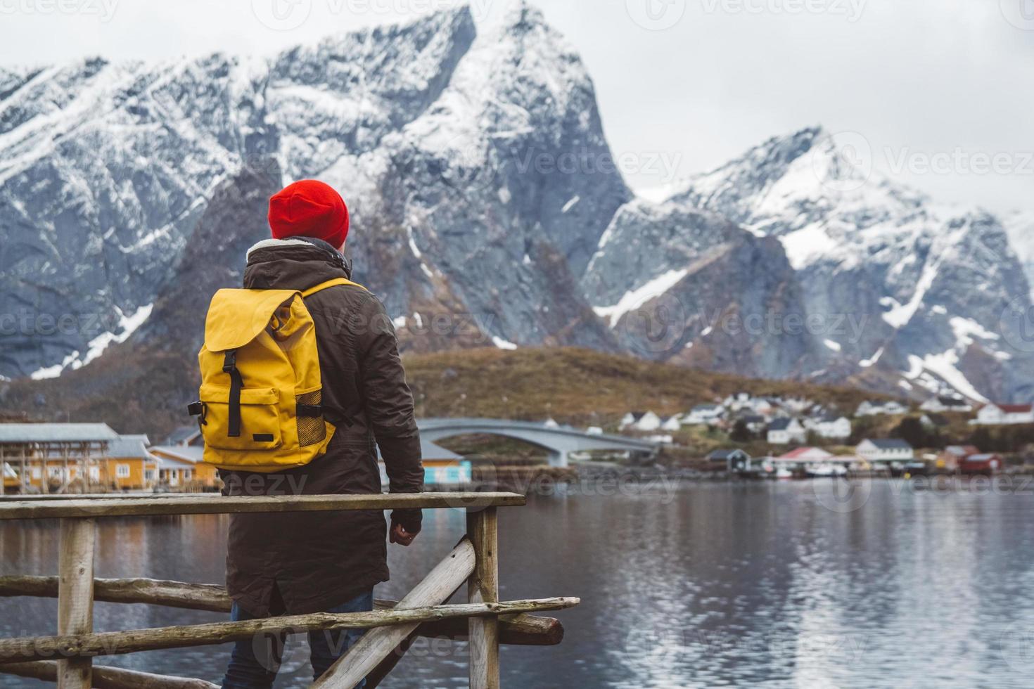 jeune homme avec un sac à dos debout sur une jetée en bois le fond des montagnes enneigées et du lac. place pour le texte ou la publicité photo