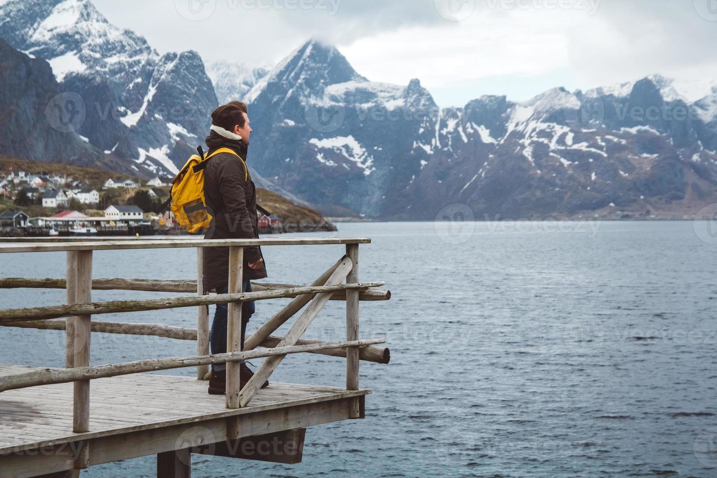 homme voyageur avec un sac à dos debout sur une jetée en bois le fond des montagnes enneigées et du lac. place pour le texte ou la publicité photo