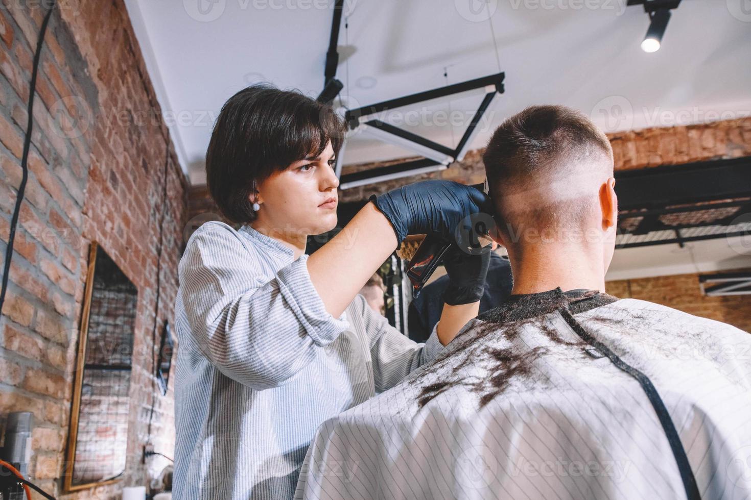 belle femme coiffeuse fait une coupe de cheveux la tête du client avec une tondeuse électrique dans un salon de coiffure. concept de publicité et de salon de coiffure. place pour le texte ou la publicité photo
