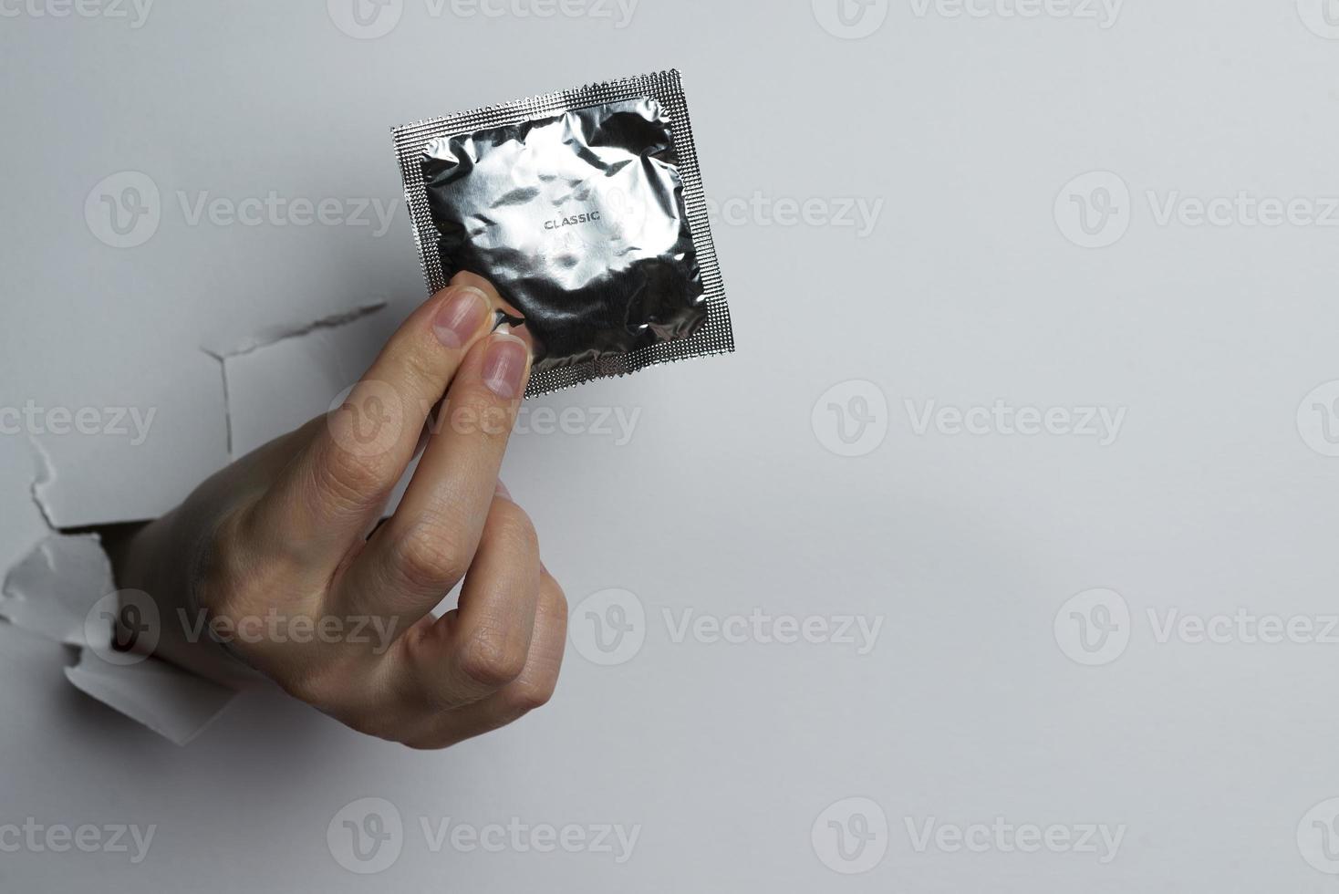 main féminine tenant un préservatif, sur fond blanc. photo