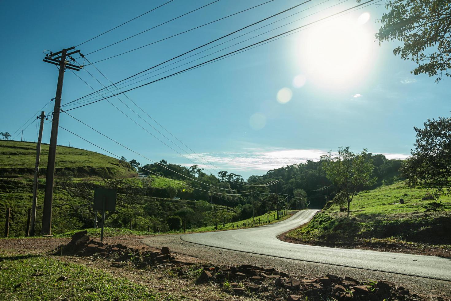route de campagne pavée à côté de la silhouette des arbres feuillus avec la lumière du soleil sur une pente couverte de prairie verte près de pardinho. un petit village rural dans la campagne de l'état de sao paulo. photo