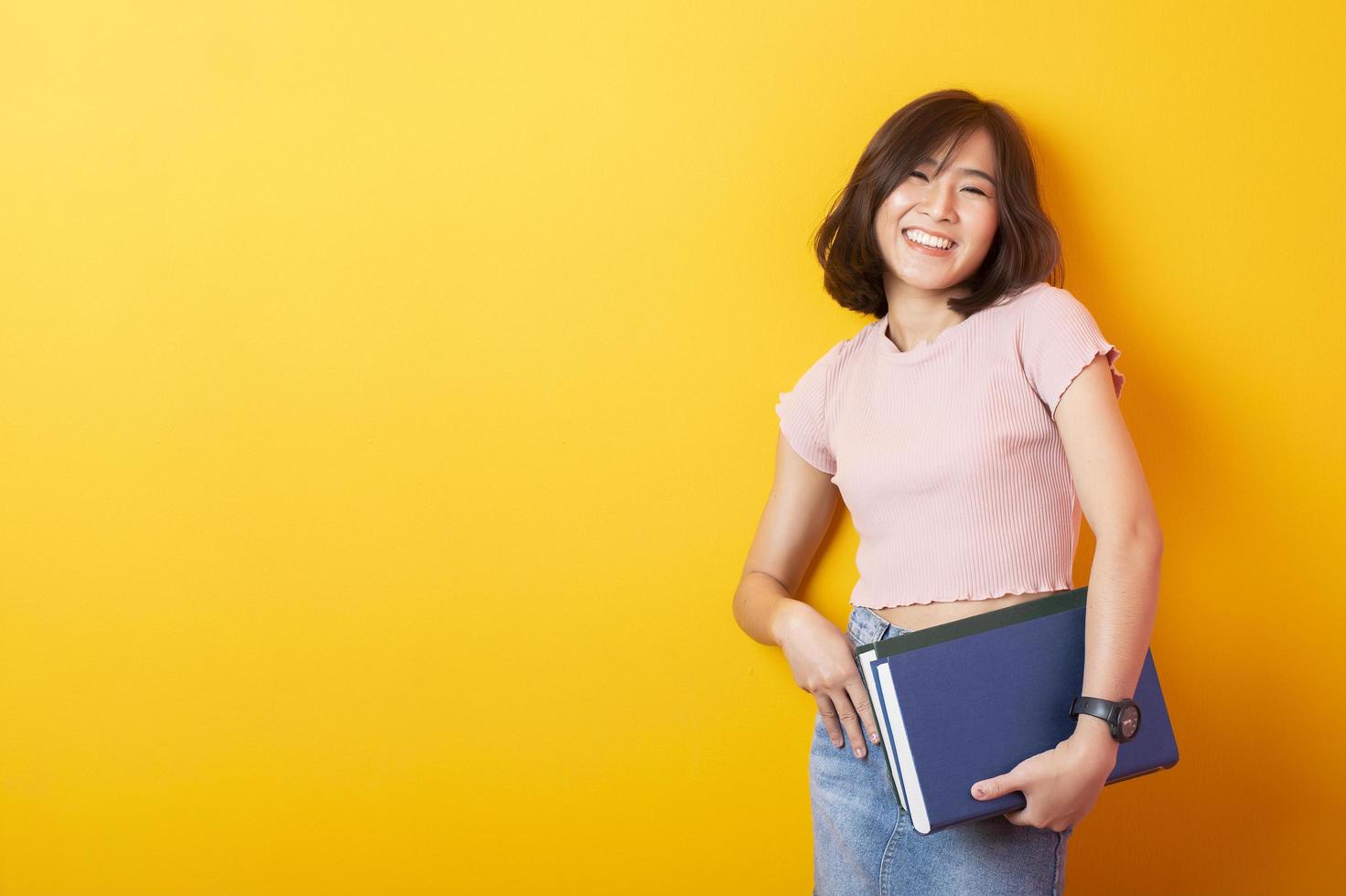 belle femme asiatique étudiant universitaire heureux sur fond jaune photo