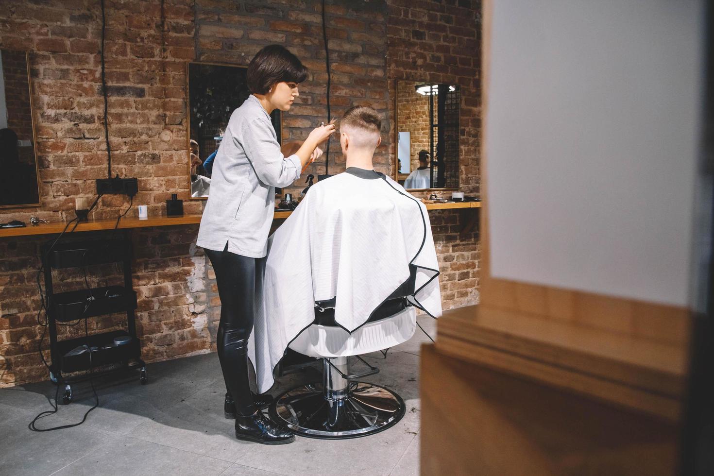 belle coiffeuse coupe les cheveux du client avec des ciseaux dans un salon de coiffure. concept de publicité et de salon de coiffure photo