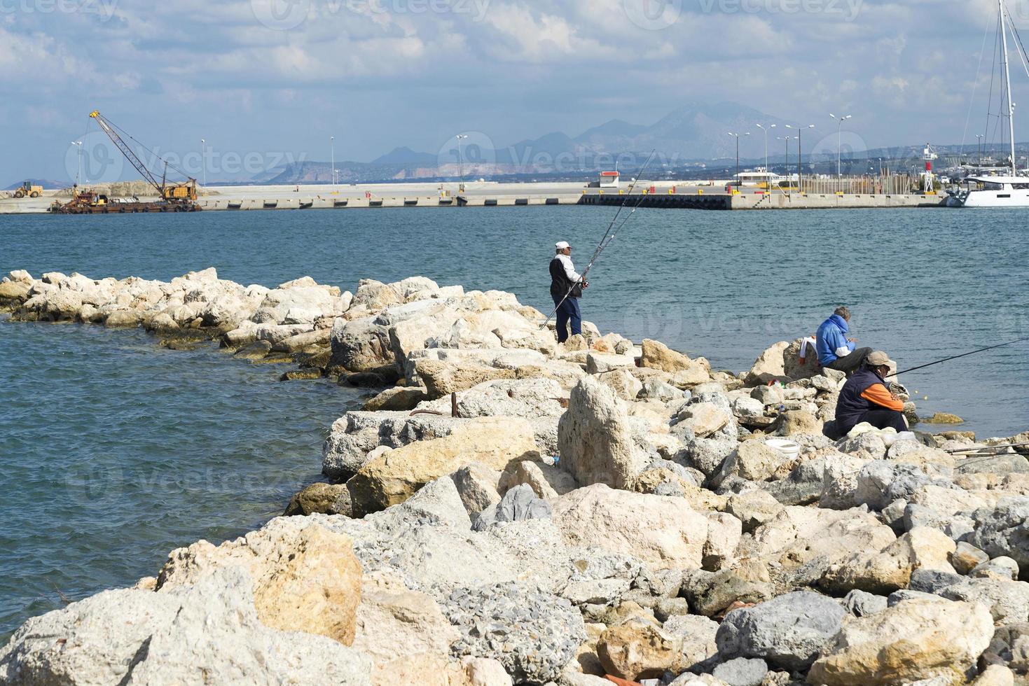 le pêcheur dans un gilet et un chapeau pêchant sur des pierres dans les vagues de la mer photo