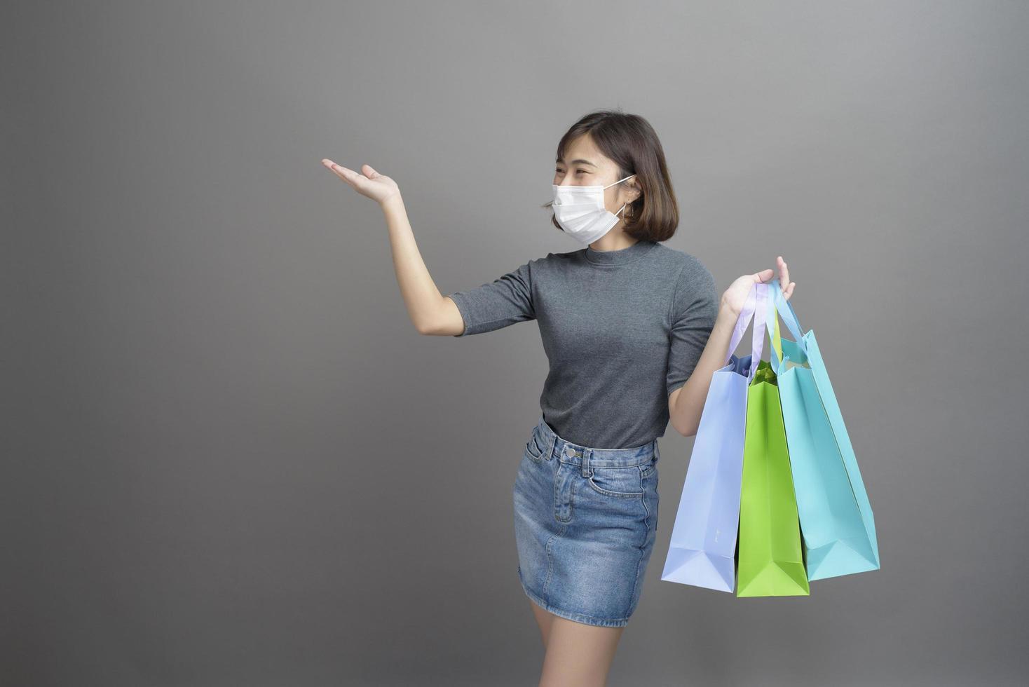 Portrait d'une belle jeune femme asiatique portant un mak chirurgical tient une carte de crédit et un sac à provisions coloré isolé sur fond gris studio photo