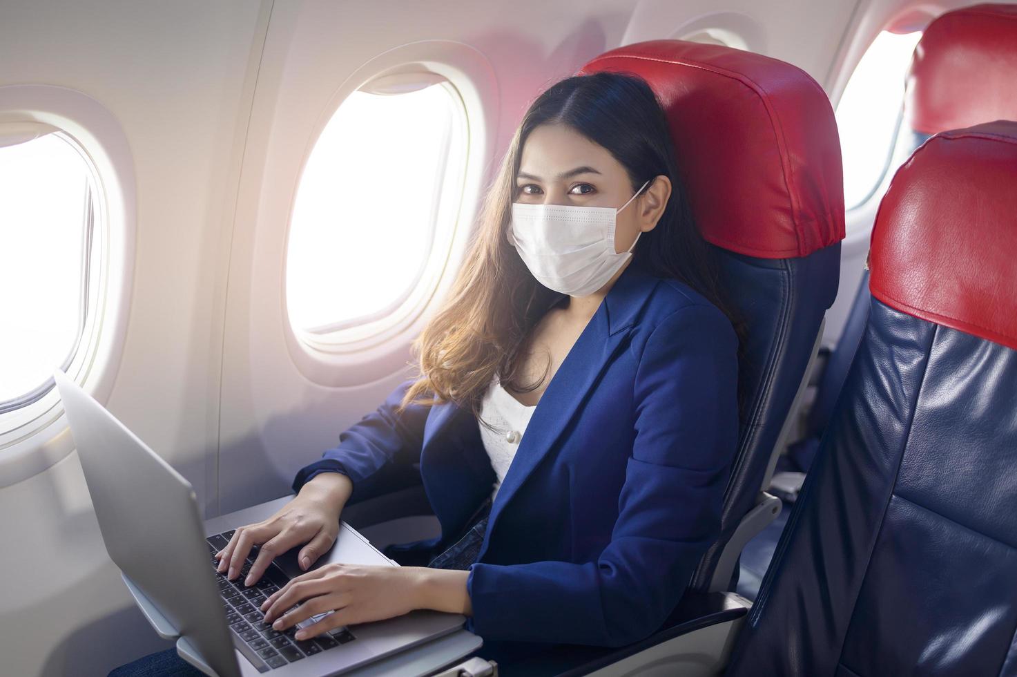 une jeune femme d'affaires portant un masque facial utilise un ordinateur portable à bord, nouveau voyage normal après le concept de pandémie de covid-19 photo