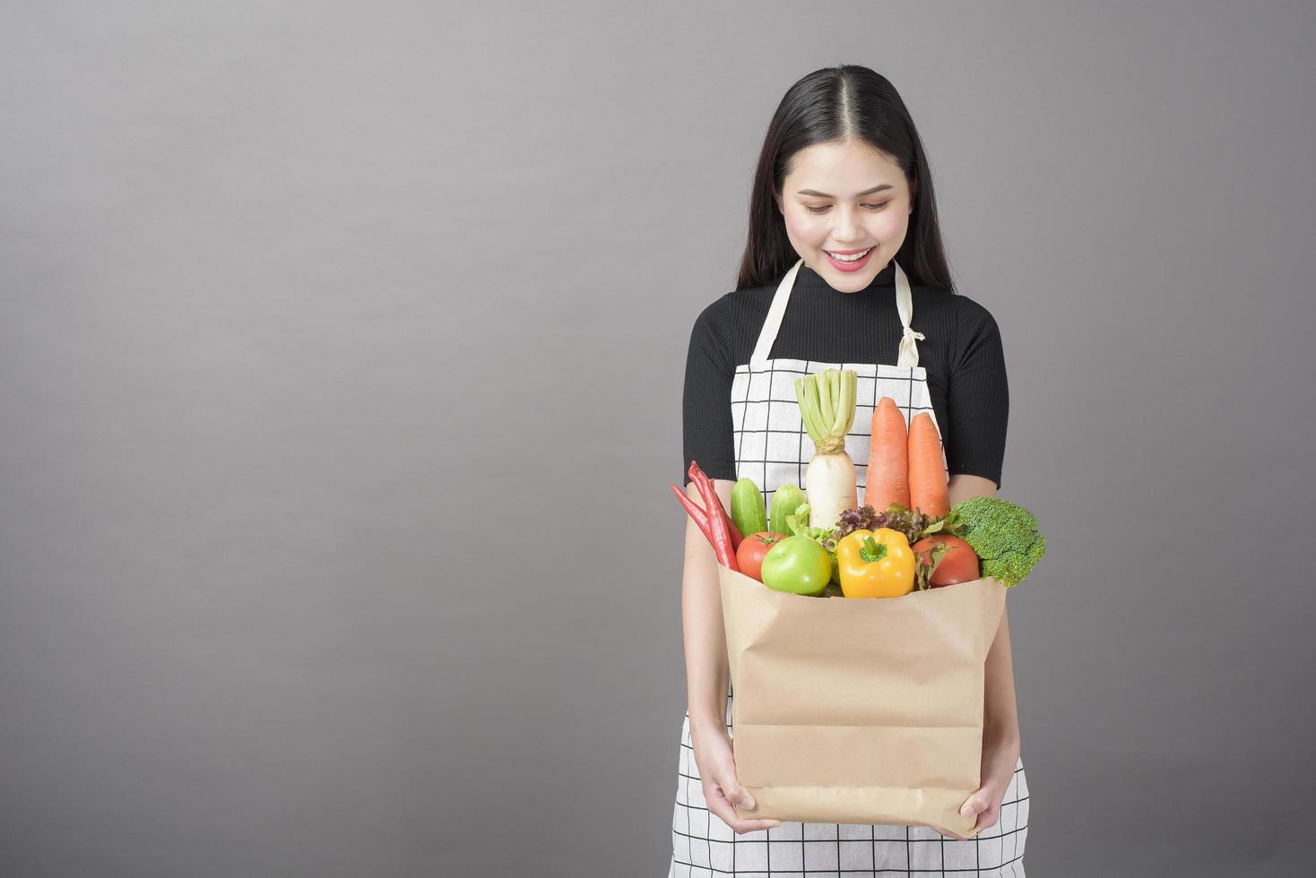 Portrait de belle jeune femme avec des légumes dans un sac d'épicerie en studio fond gris photo