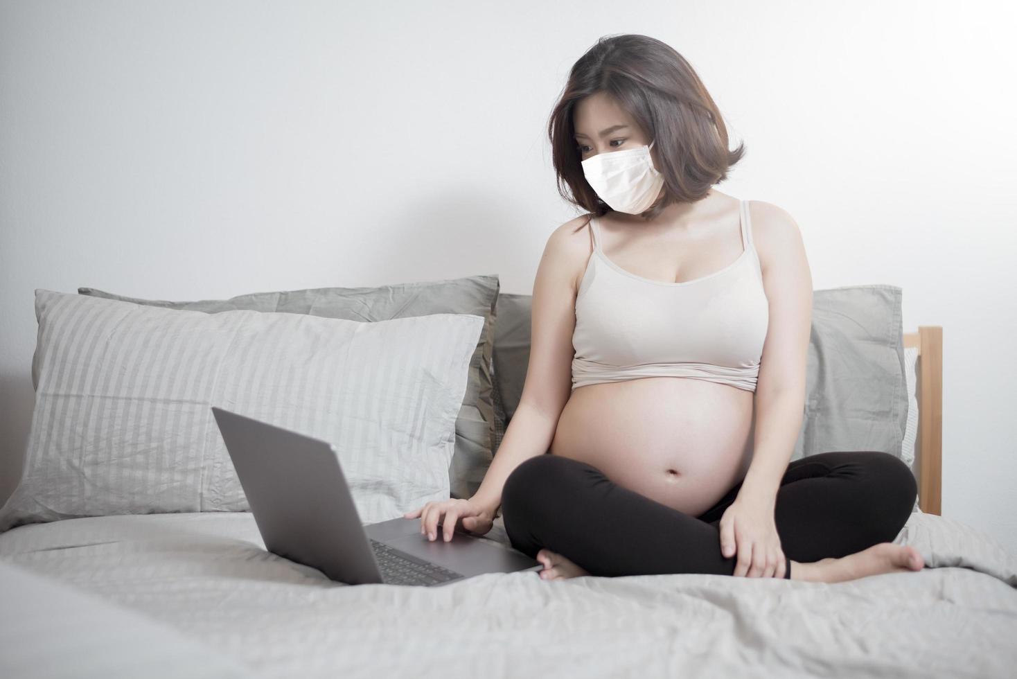 belle femme enceinte asiatique porte un masque de protection dans sa maison, concept de protection contre les coronavirus photo
