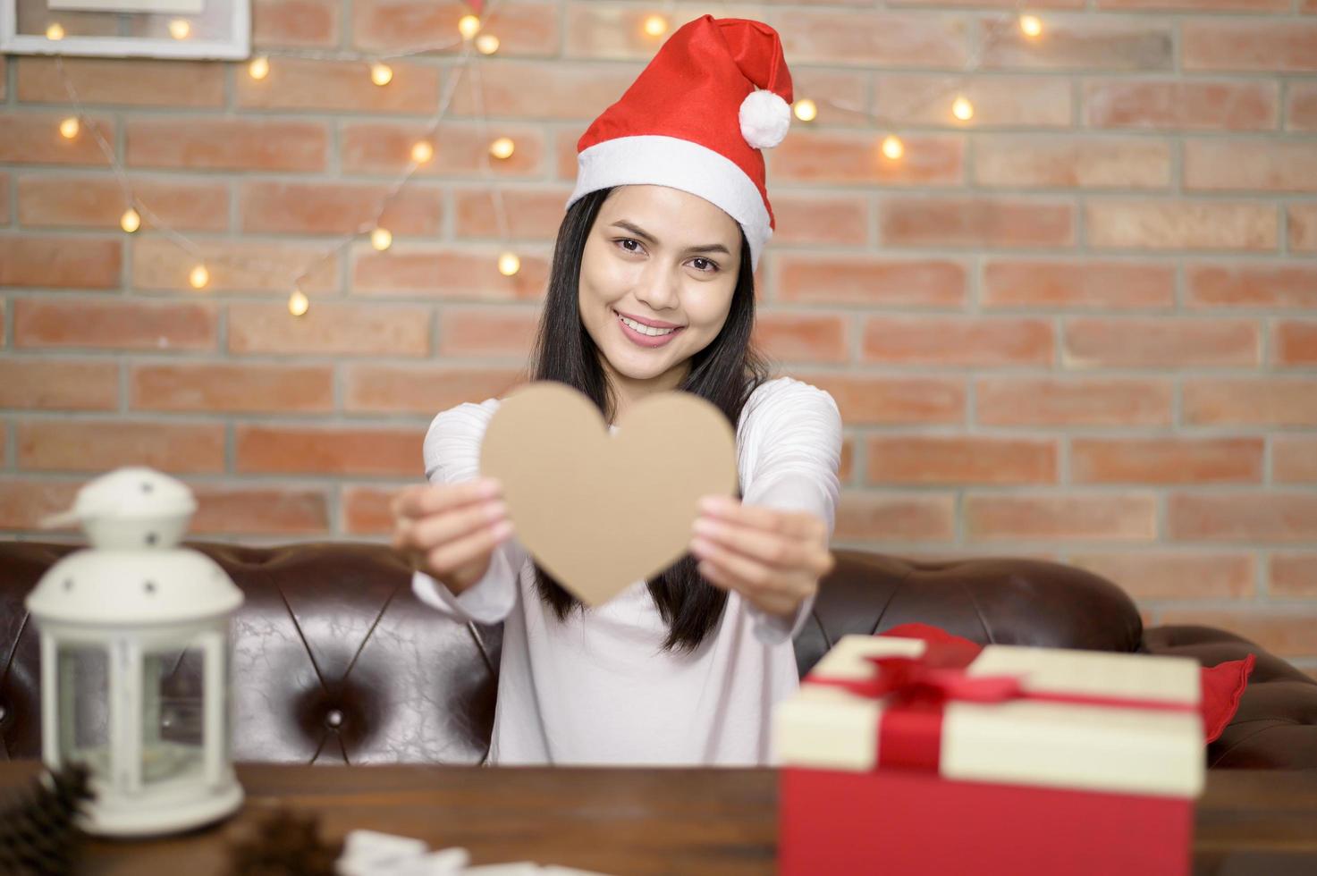 jeune femme souriante portant un chapeau de père noël rouge montrant un modèle en forme de coeur le jour de noël, concept de vacances. photo