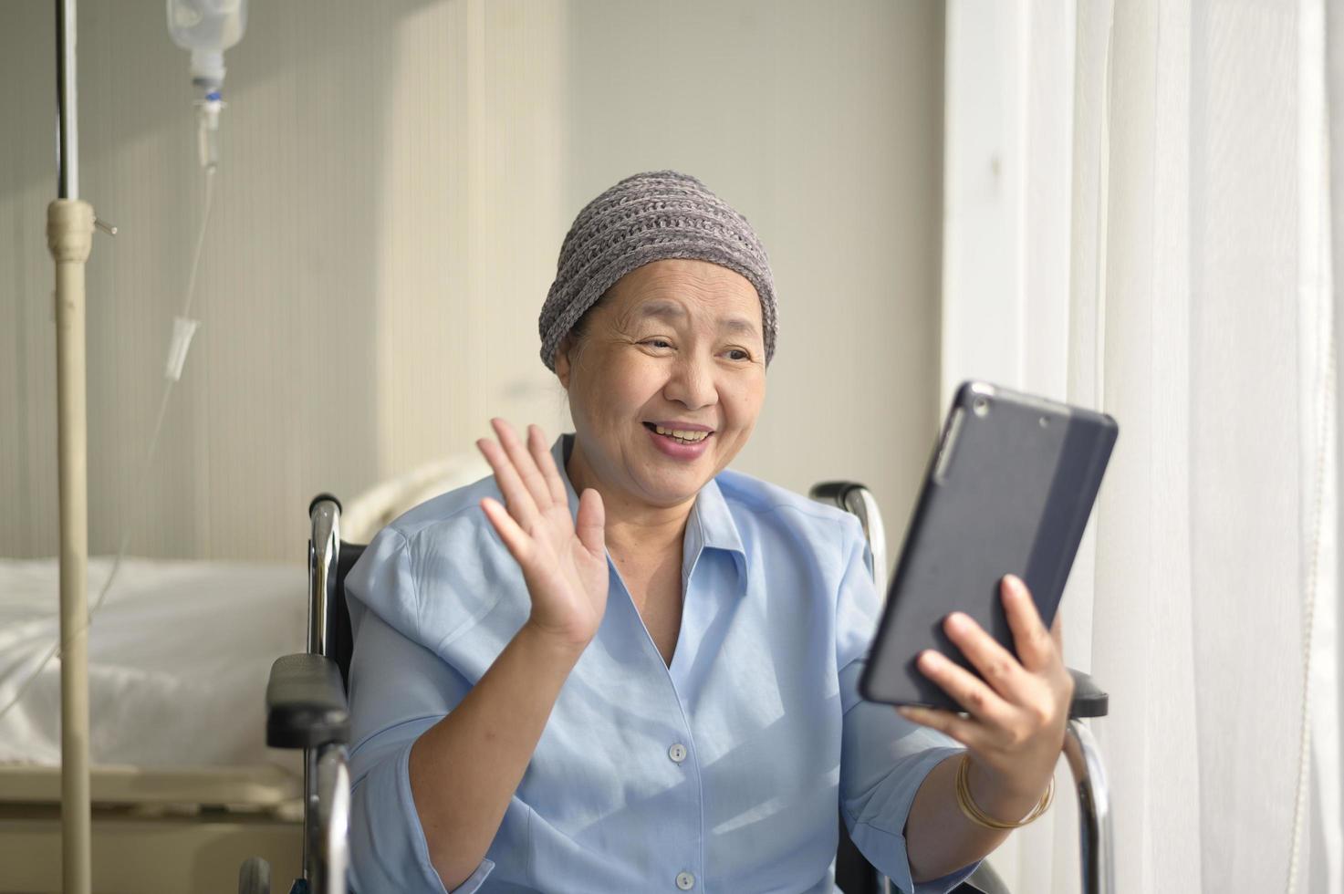 femme cancéreuse portant un foulard faisant un appel vidéo sur un réseau social avec sa famille et ses amis à l'hôpital. photo