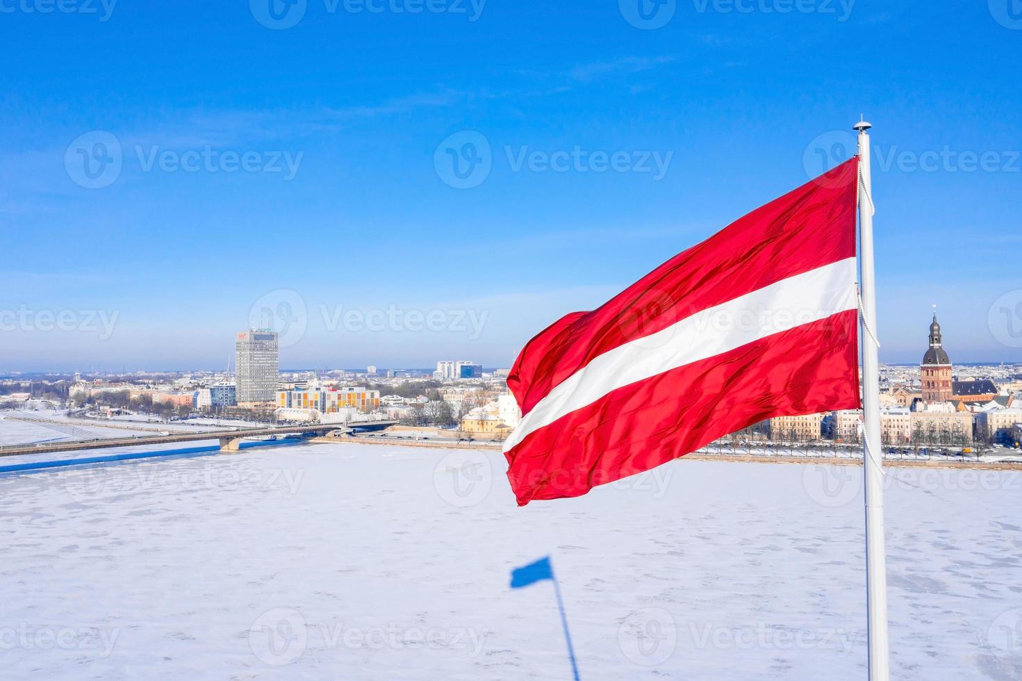 drapeau letton sur la rivière gelée daugava avec une vieille ville de riga en arrière-plan. photo