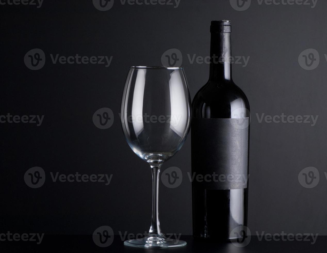 bouteille de vin rouge avec un verre sur fond noir photo