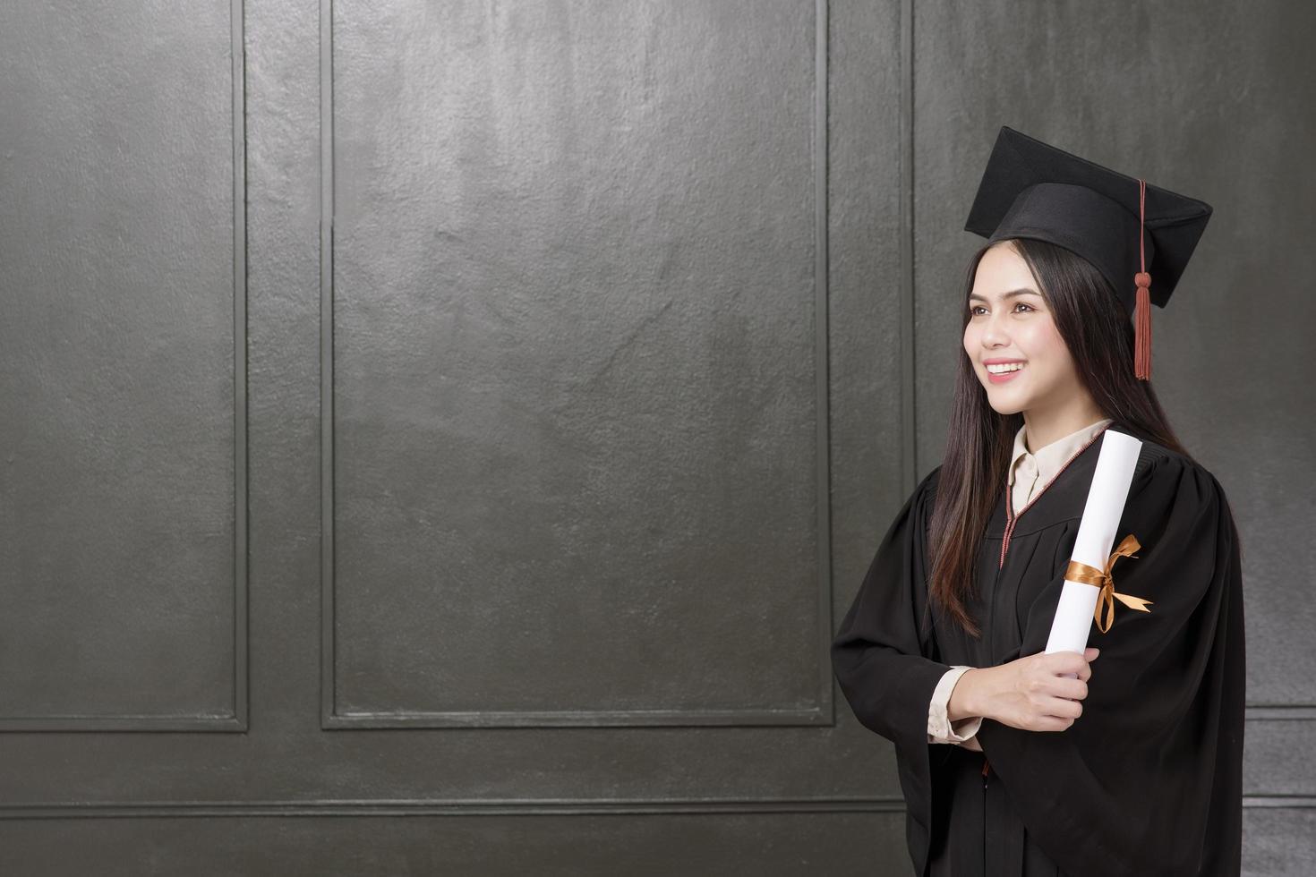 Portrait de jeune femme en robe de graduation souriant et acclamant sur fond noir photo