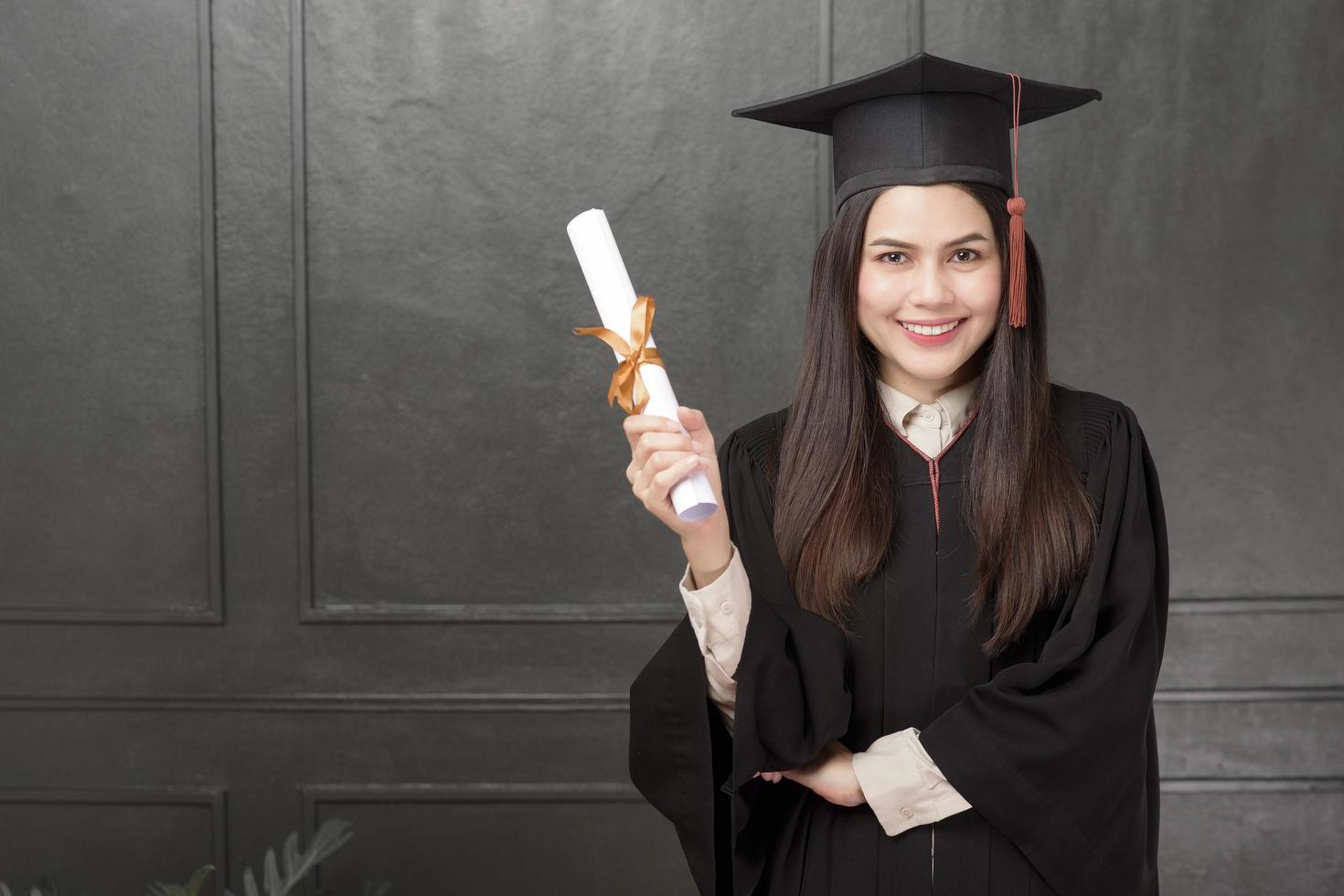 Portrait de jeune femme en robe de graduation souriant et acclamant sur fond noir photo