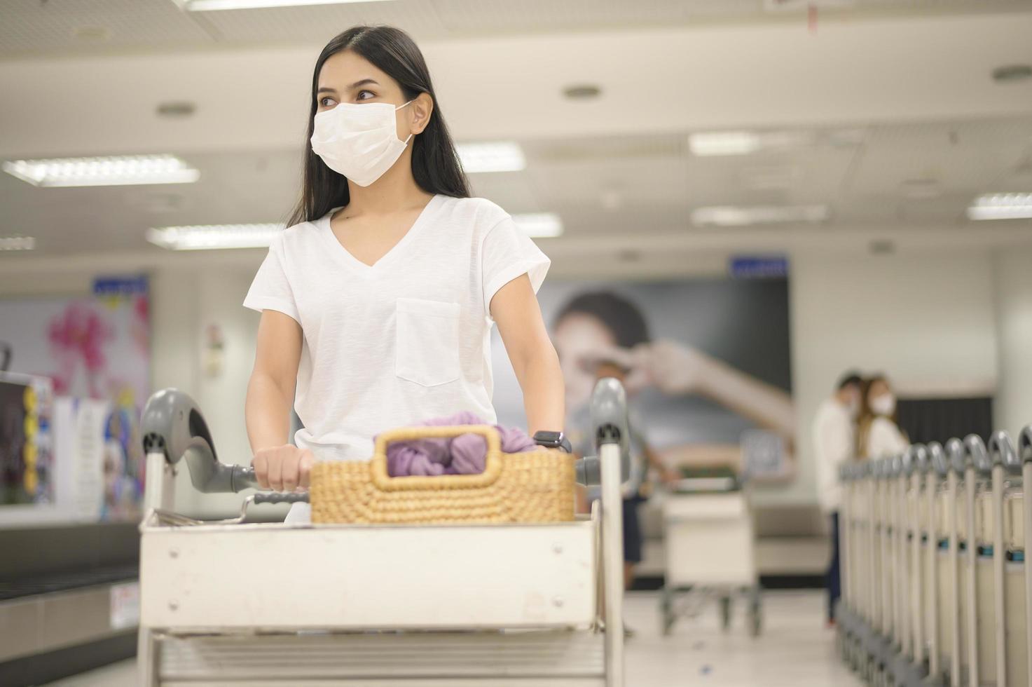 une femme en voyage portant un masque de protection à l'aéroport avec des bagages sur un chariot, voyage sous la pandémie de covid-19, voyages de sécurité, protocole de distanciation sociale, nouveau concept de voyage normal photo