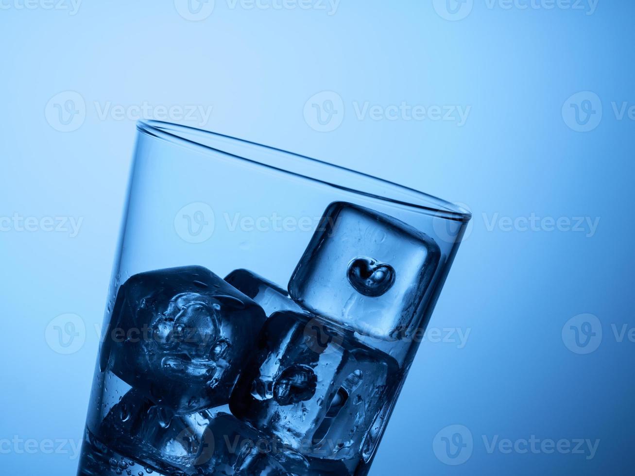 haut d'un verre d'eau avec des glaçons sur fond bleu clair photo