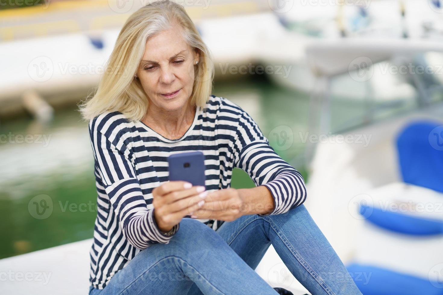 femme âgée utilisant son smartphone assis dans un port maritime. photo