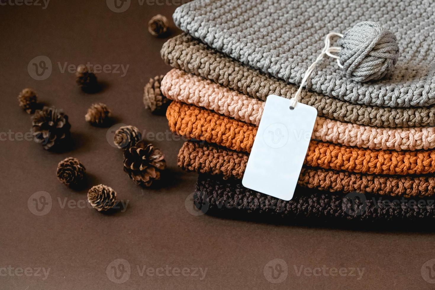 pile de tissu tricoté à partir de fils de couleurs marron, orange, gris avec une étiquette de prix vide sur fond marron. copie, espace vide pour le texte photo