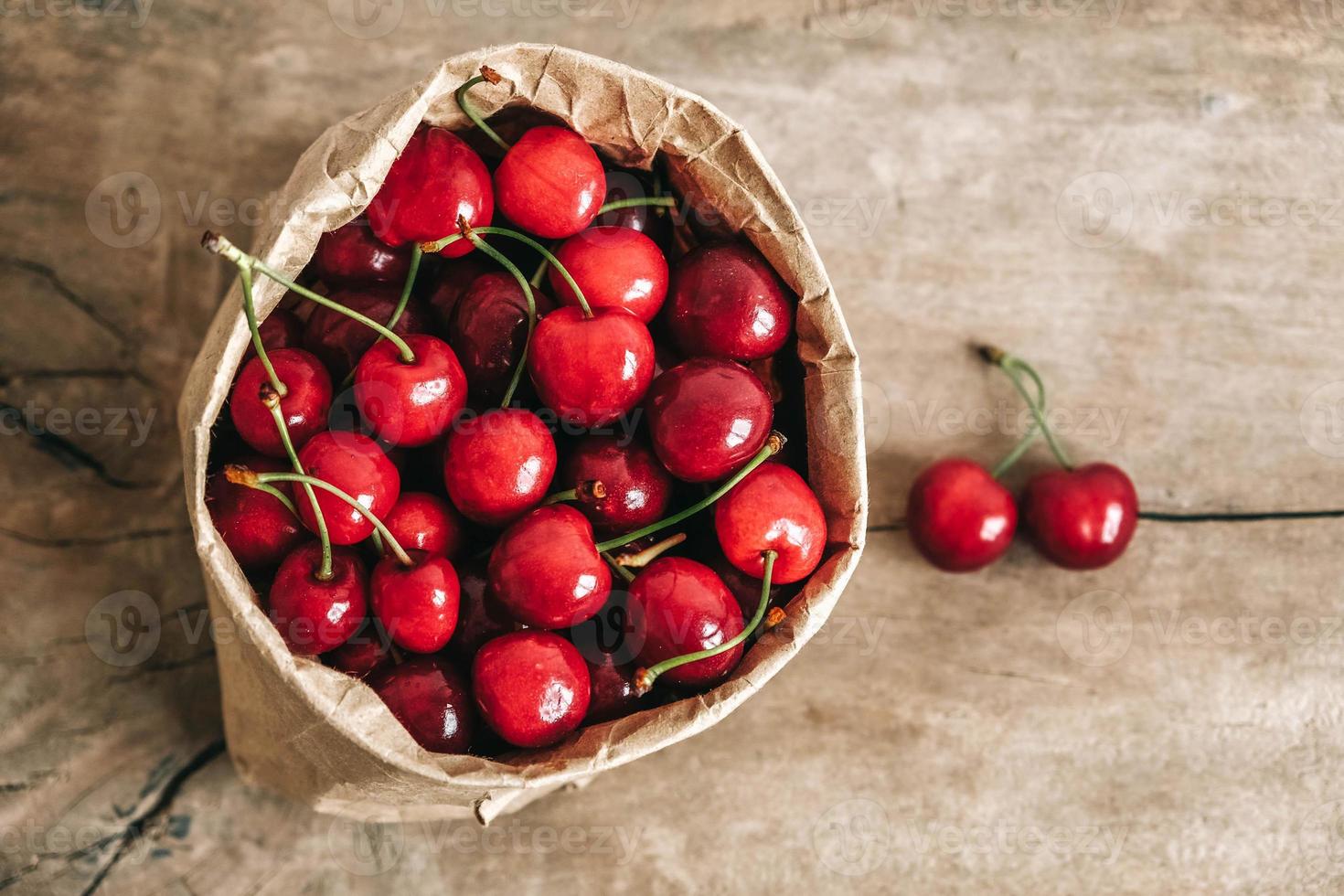 cerises mûres fraîches dans un sac en papier sur fond en bois. vue de dessus. copie, espace vide pour le texte photo