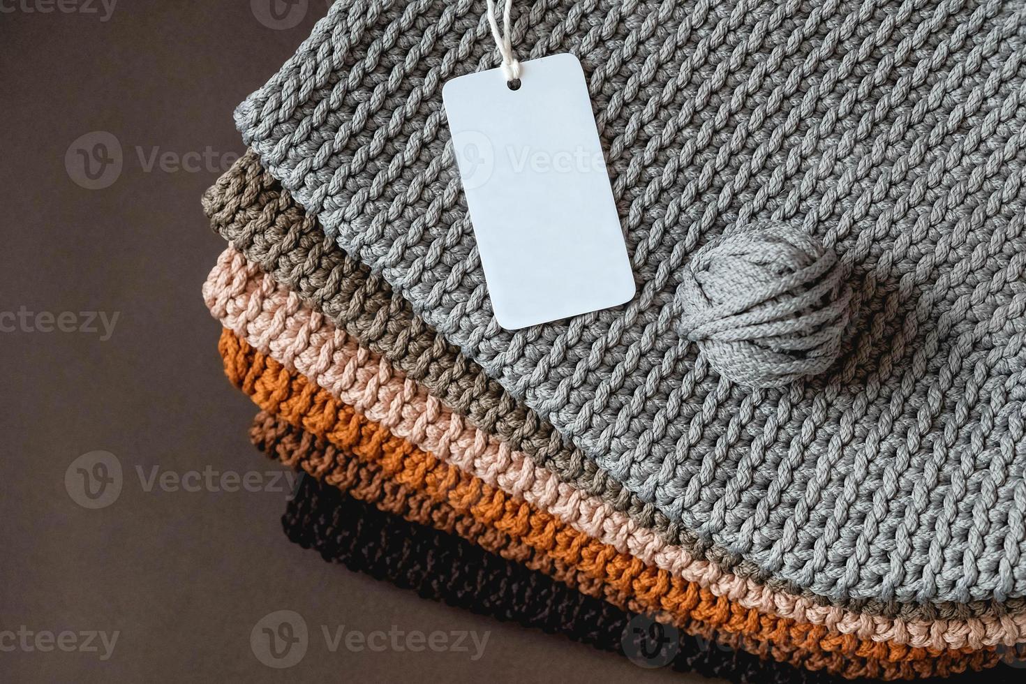 pile de tissu tricoté à partir de fils de couleurs marron, orange, gris avec une étiquette de prix vide sur fond marron photo