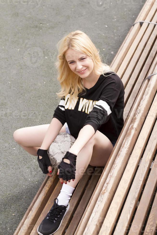 la fille est assise sur le banc du terrain de football avec le ballon. photo