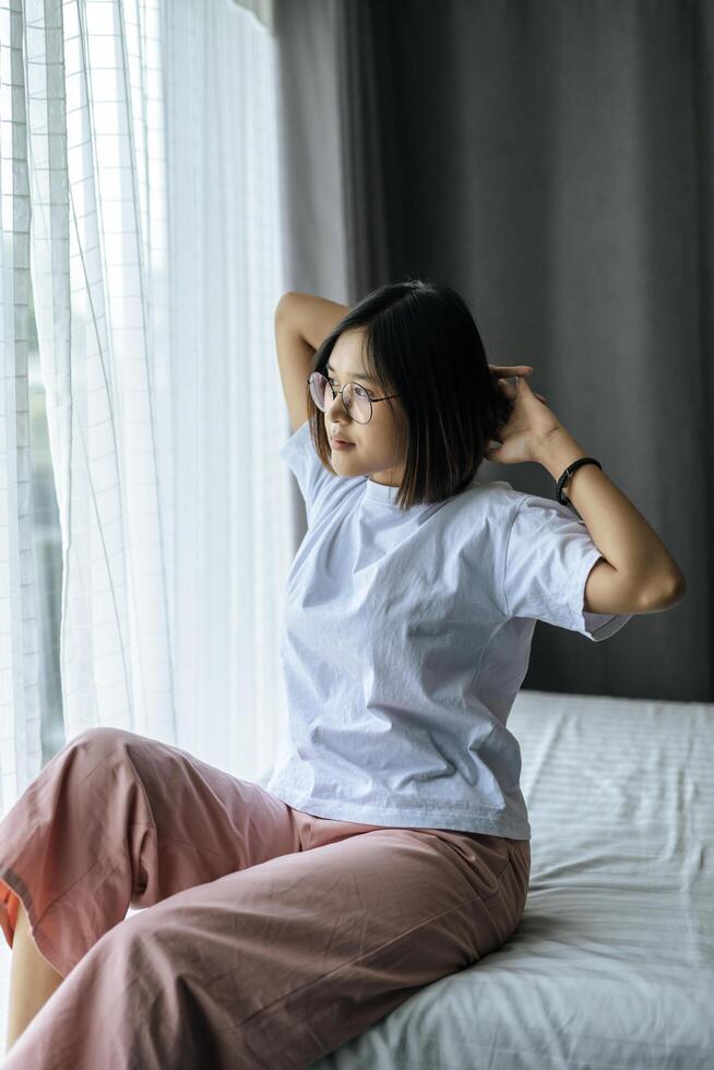 une femme en chemise blanche assise sur le lit et levant les deux bras. photo