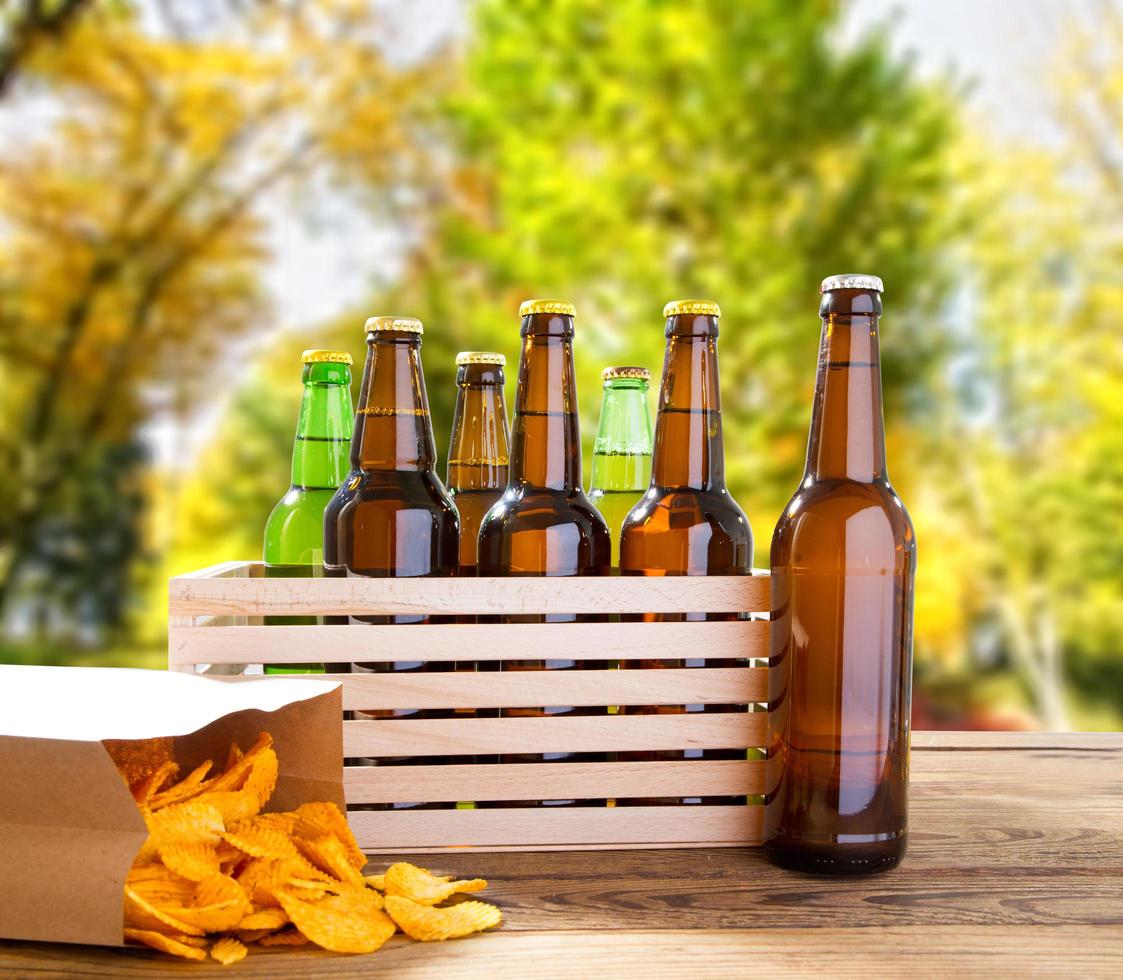 bouteilles de bière et croustilles sur table en bois avec parc flou sur fond, bouteille colorée, concept de nourriture et de boisson, mise au point sélective, espace de copie photo