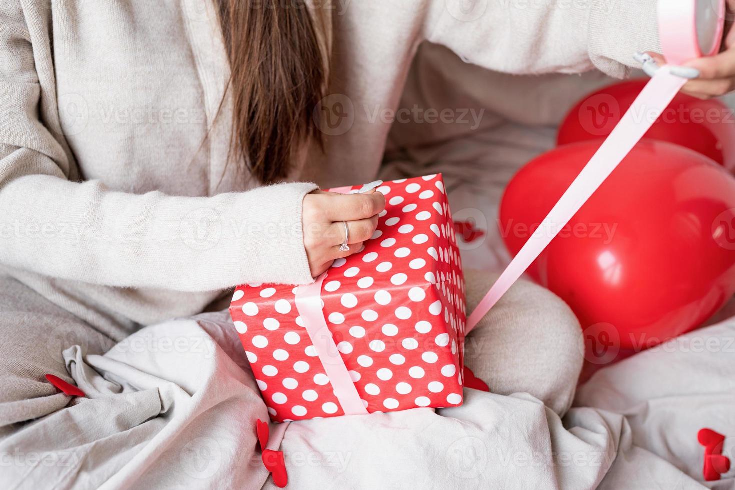 jeune femme drôle assise dans le lit célébrant la saint valentin emballant les cadeaux photo