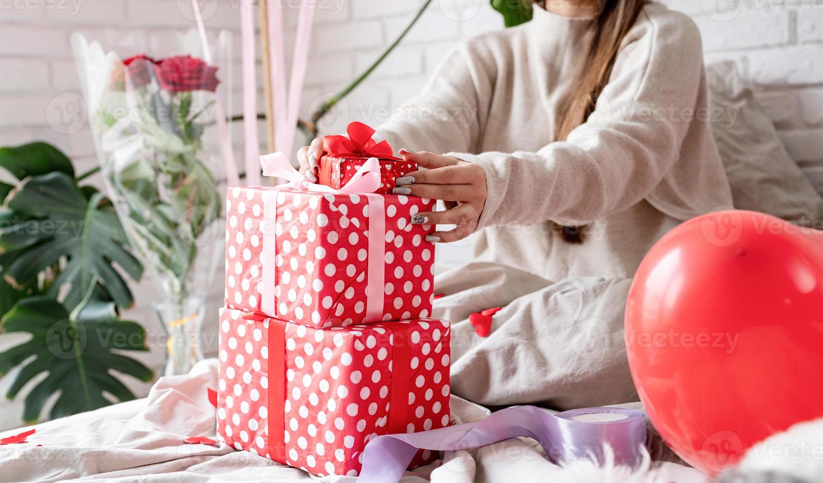 jeune femme drôle assise dans le lit célébrant la saint valentin emballant les cadeaux photo