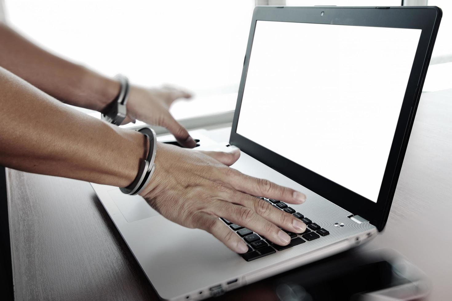 main d'homme d'affaires menotté au bureau en bois avec ordinateur portable et tablette numérique et stylet et téléphone intelligent comme concept de cybercriminalité photo