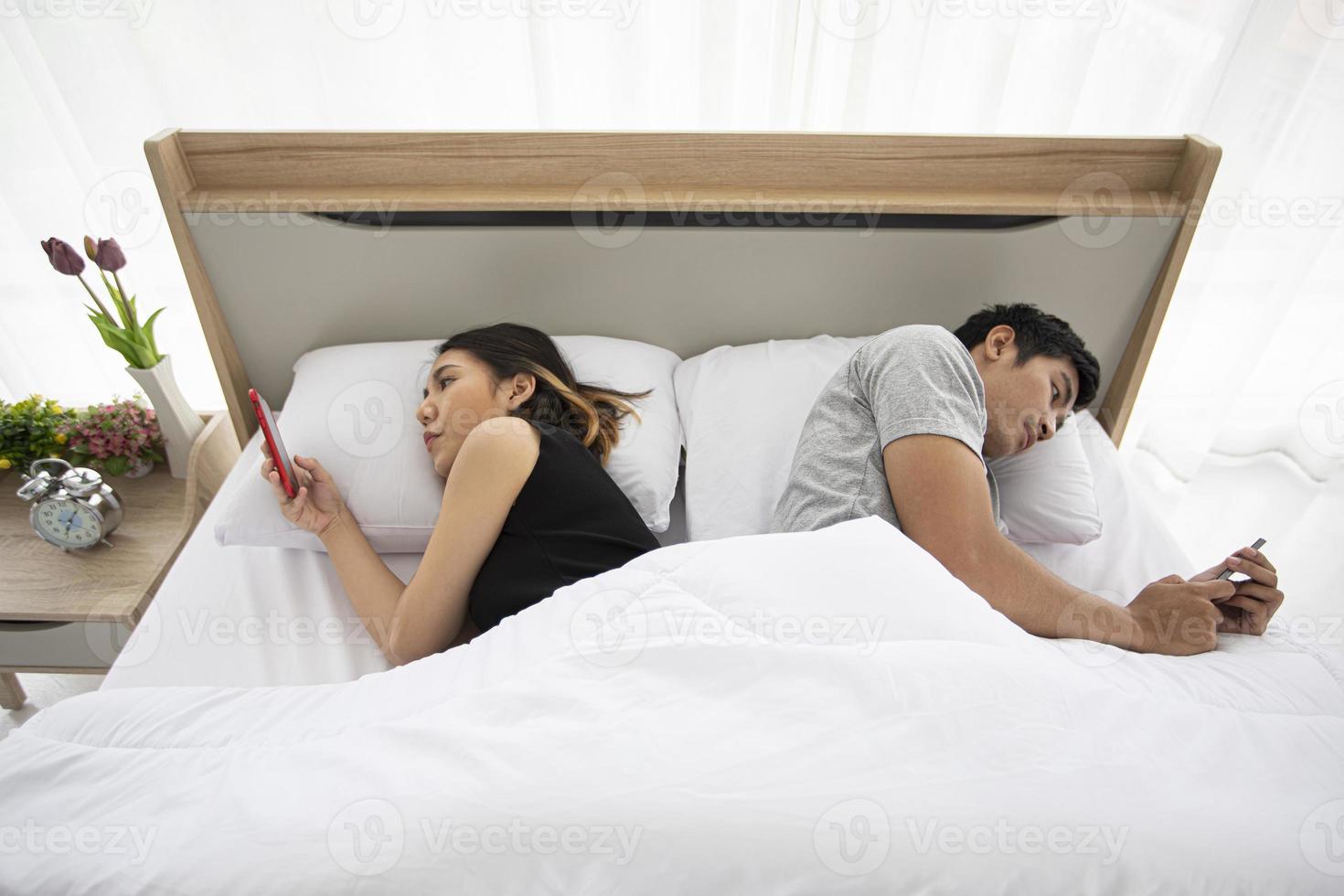 Couple d'amoureux asiatiques allongés sur leur téléphone mobile sur le lit photo