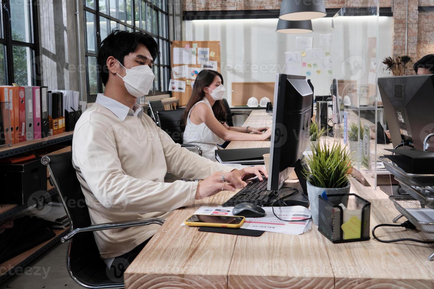 équipe de trois collègues, collègues masqués travaillant dans un nouveau bureau normal. protection covid-19 par cloison dégagée, bureau de travail, distanciation sociale pour la santé pandémique, prévention des maladies. photo