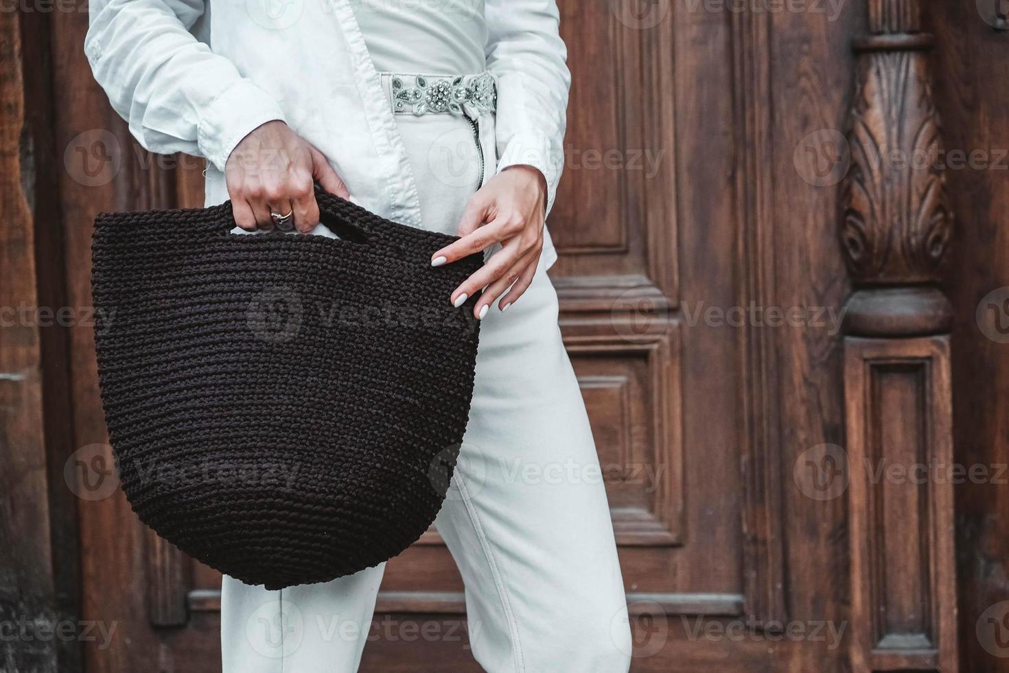 femme portant des vêtements blancs, tenant un sac tricoté sur fond de vieilles portes en bois photo