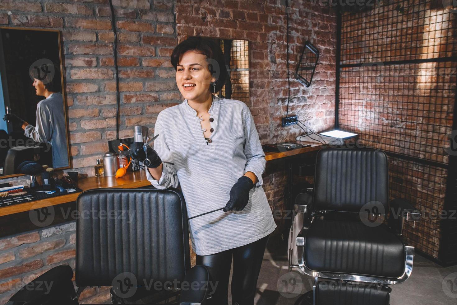 belle jeune femme de coiffure avec des ciseaux à la main sur un fond de mur de briques. concept publicitaire de salon de coiffure. place pour le texte ou la publicité photo