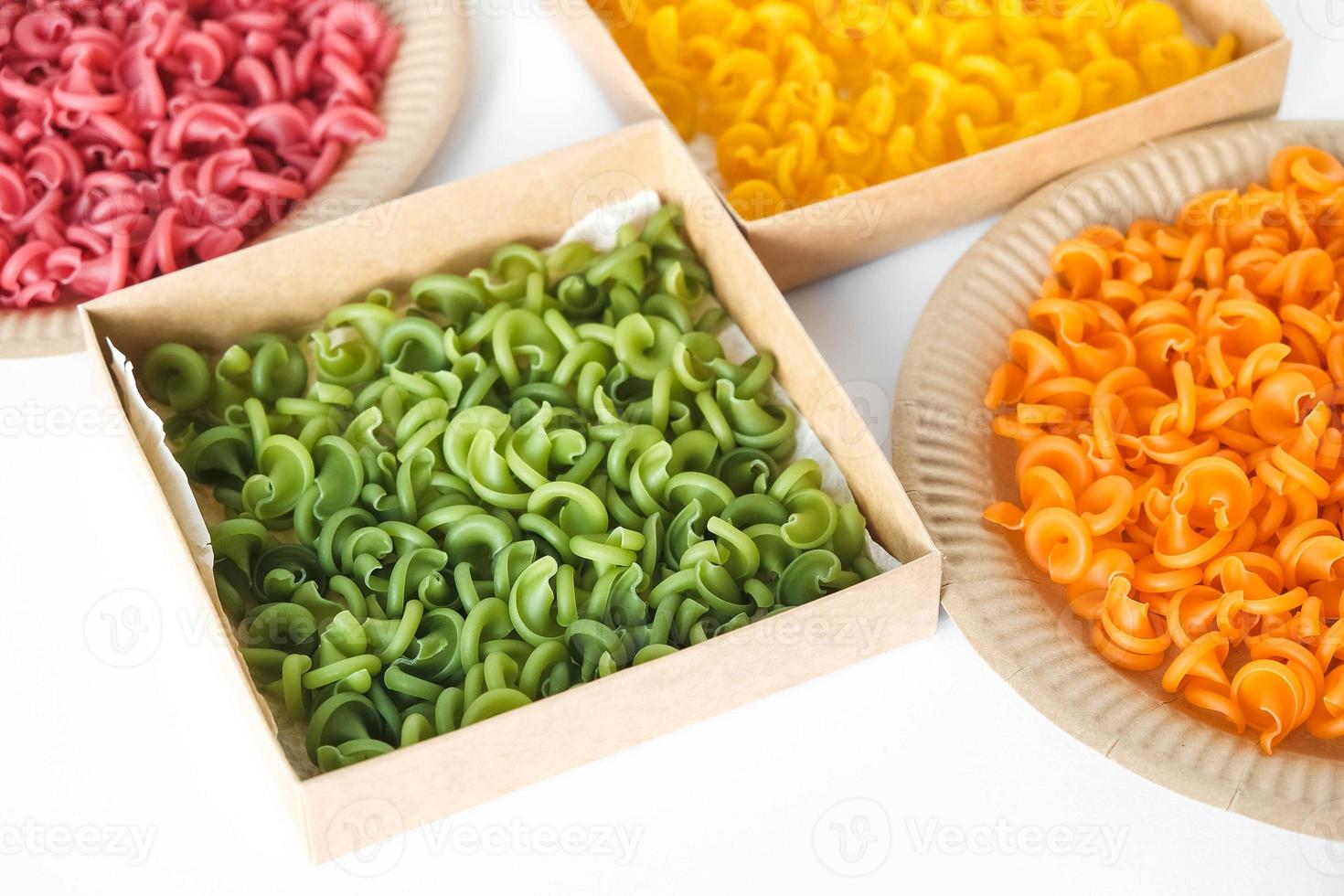 pâtes multicolores dans des assiettes et des boîtes en papier kraft jetables sur fond blanc. vue de dessus. copie, espace vide pour le texte photo