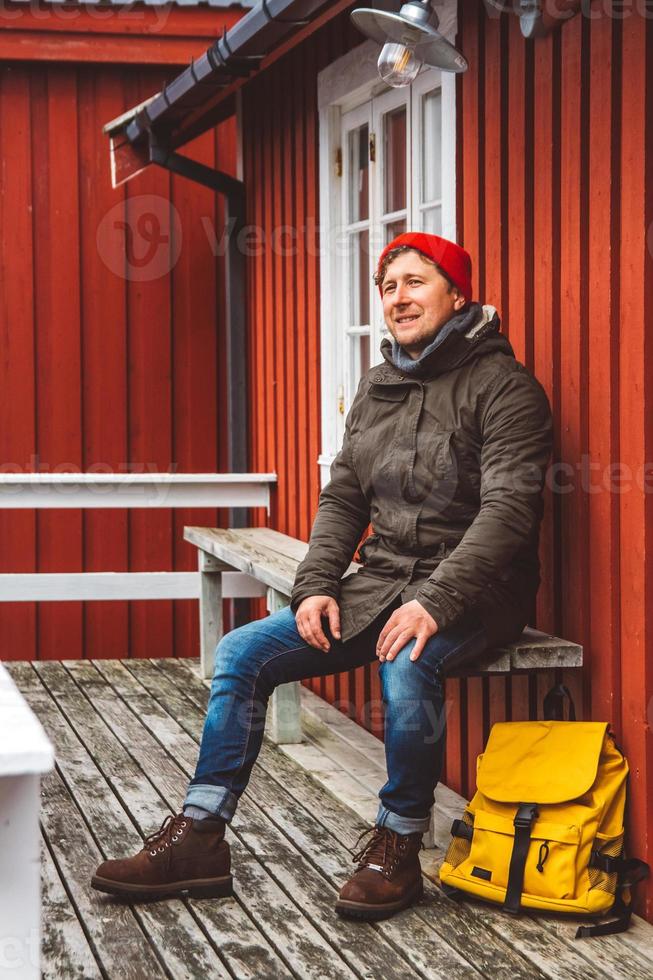 homme voyageur avec un sac à dos jaune portant est assis près de la maison en bois de couleur rouge photo