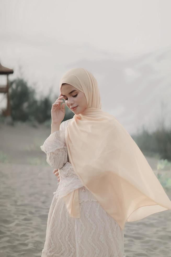 beau modèle féminin islamique portant la mode hijab, une robe de mariée moderne pour femme musulmane se promène le long du sable et de la mer. un modèle de fille asiatique utilisant le hijab s'amusant à la plage. photo avant mariage