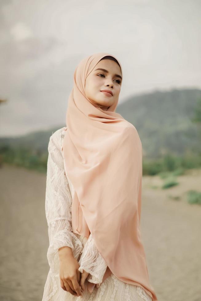 beau modèle féminin islamique portant la mode hijab, une robe de mariée moderne pour femme musulmane se promène le long du sable et de la mer. un modèle de fille asiatique utilisant le hijab s'amusant à la plage. photo avant mariage