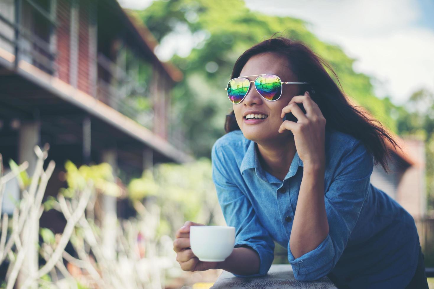 jeune femme hipster parlant au téléphone tout en tenant une tasse de café le matin et souriant. concept de vacances relaxantes. photo