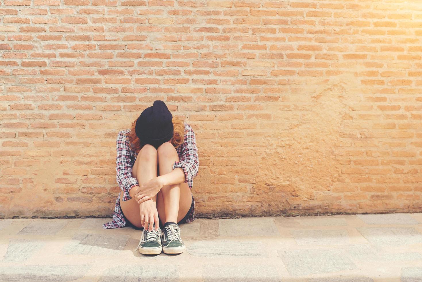 jeune femme triste assise contre le mur de briques seul. photo