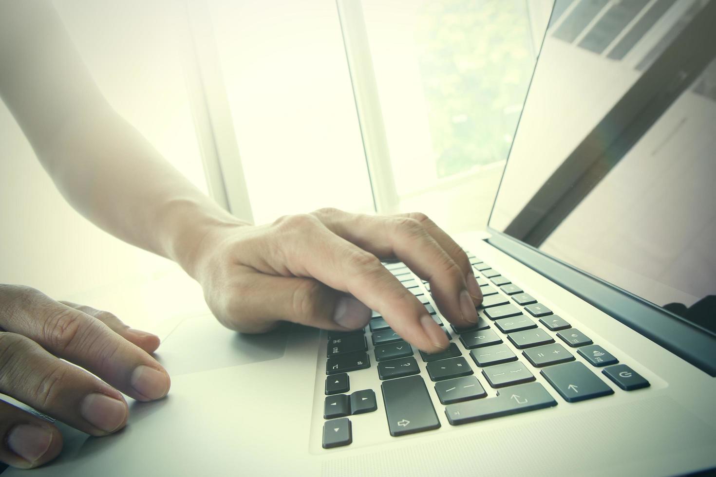 Gros plan de la main de l'homme d'affaires travaillant sur un ordinateur portable à écran blanc sur un bureau en bois comme concept photo