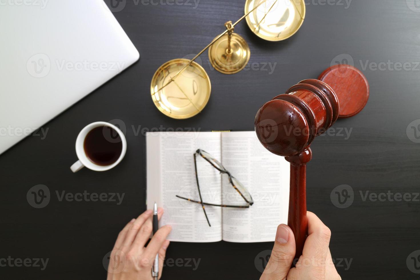 concept de justice et de droit. vue de dessus de la main du juge masculin dans une salle d'audience avec le marteau et l'échelle en laiton et l'ordinateur et le livre de la bible ouverte sur une table en bois sombre photo