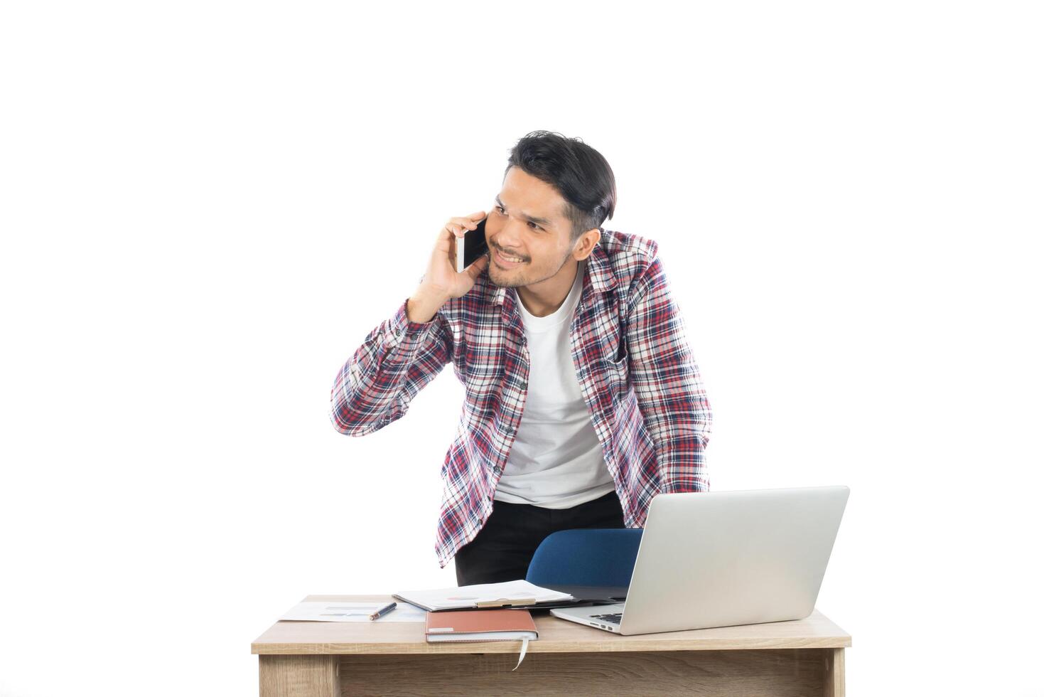 jeune homme d'affaires parlant au téléphone tout en travaillant sur un ordinateur portable au bureau, temps occupé avec le travail isolé sur fond blanc. photo