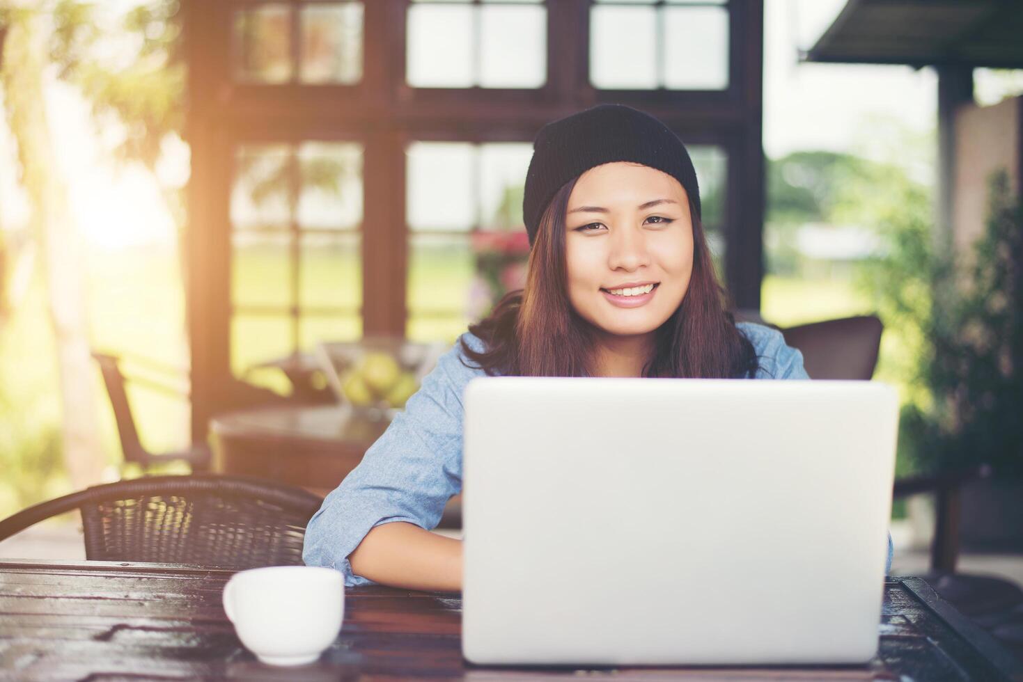 belle jeune femme hipster assise dans un café, détendez-vous et jouez avec son ordinateur portable, trouvez des informations sur le temps libre, heureux et amusant. notion de style de vie. photo