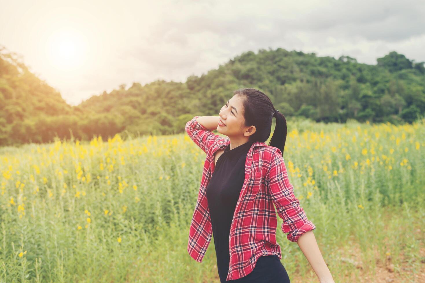 jeune femme heureuse levant les mains dans un champ de fleurs jaunes au coucher du soleil, arrière-plan vue sur la montagne. photo